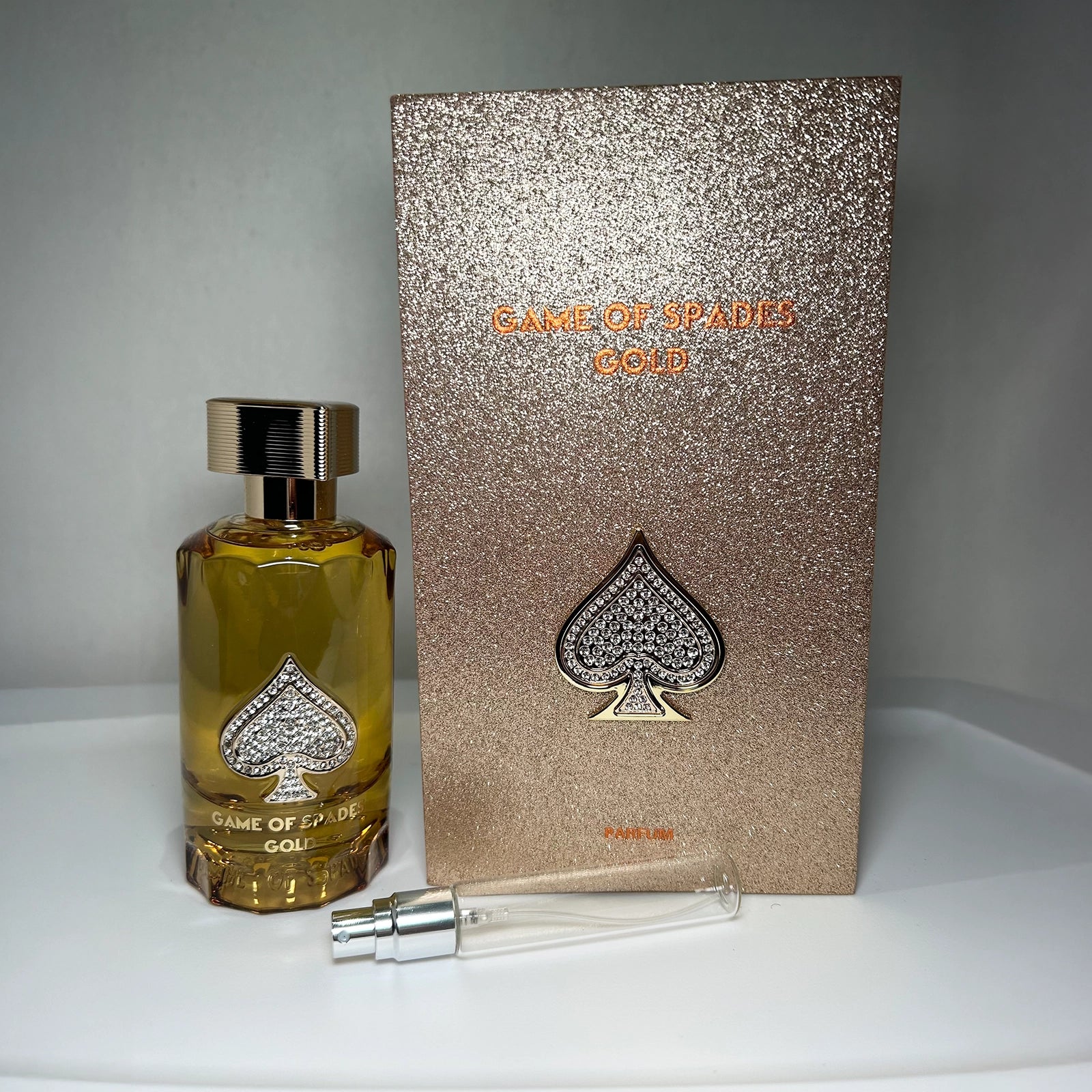 Perfume bottle and packaging with 'Game of Spades Gold' branding on a gray background